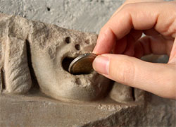 Eine Hand steckt eine Münze on den Mund eines römischen Wasserspeiers